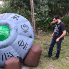 Man in suit near crashed futuristic spacecraft in forest.