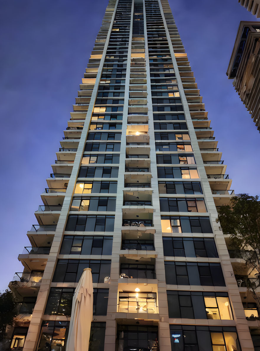 Tall residential skyscraper at dusk with illuminated windows against deep blue sky