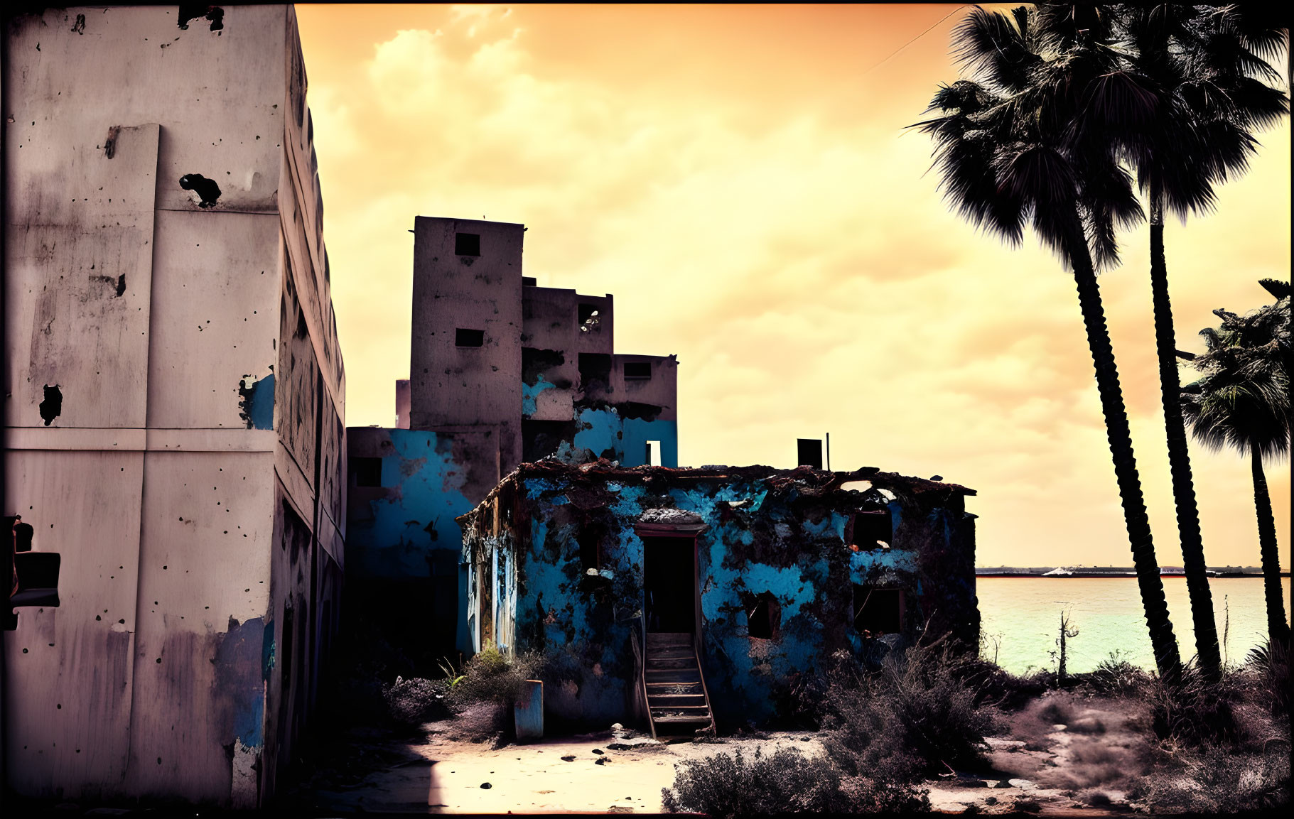 Abandoned building with peeling blue paint under orange sky and palm trees.