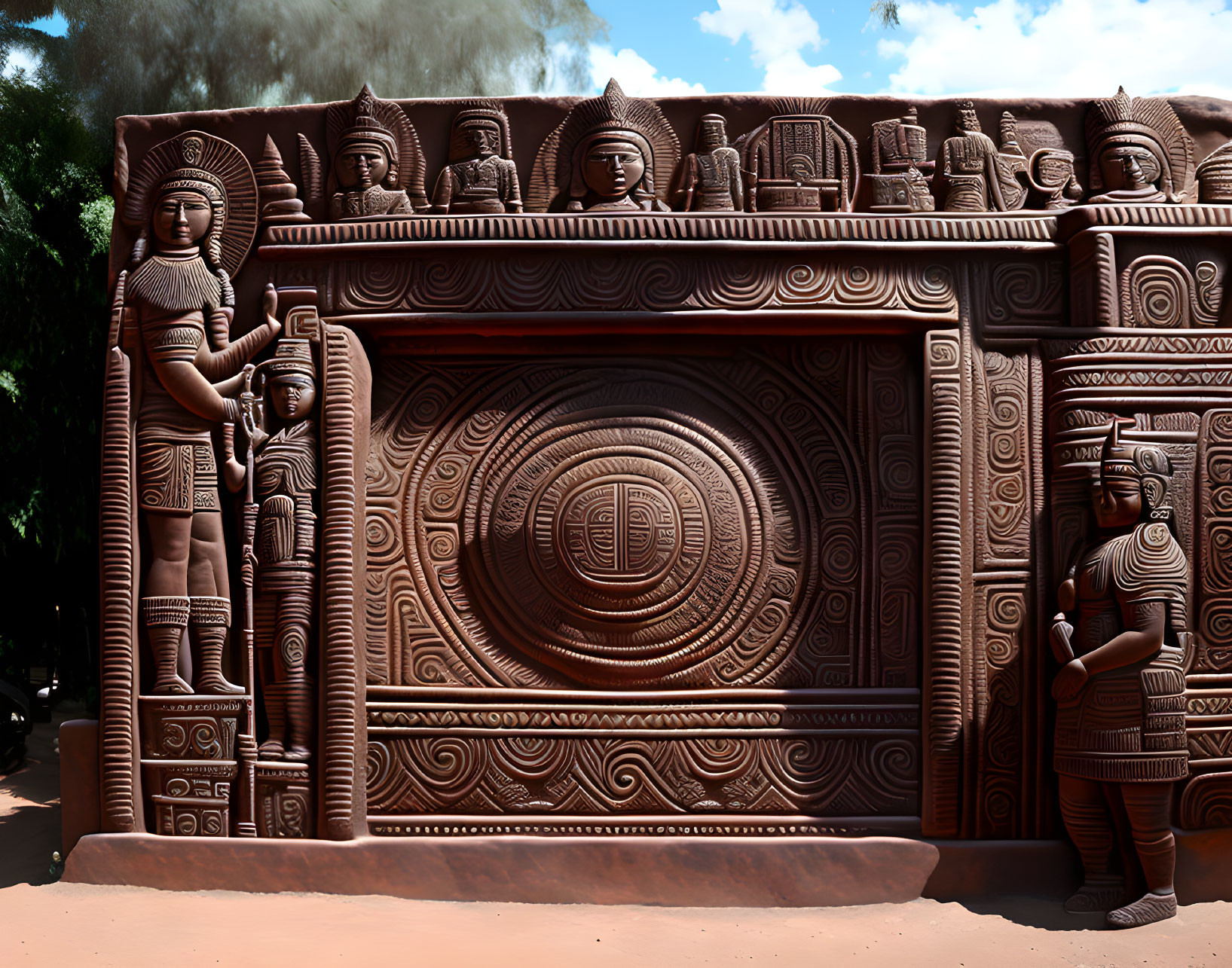 Sculpted wall with circular patterns, flanked by traditional statues under sunny sky