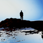 Silhouette of person on rocky shore under deep blue sky