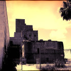 Abandoned building with peeling blue paint under orange sky and palm trees.