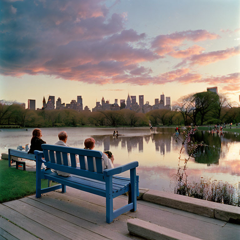 People on Blue Bench by Lake in Park at Sunset Facing City Skyline