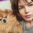 Vibrant portrait of woman with striking makeup beside detailed Pomeranian against abstract background