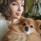 Stylized portrait of woman with curly hair in green floral outfit holding Pomeranian dog against leaf