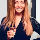 Smiling woman with colorful wavy hair holding champagne glass in dark blue outfit