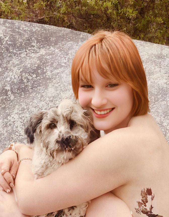 Red-Haired Woman Embracing Scruffy Dog Outdoors on Stone Bench