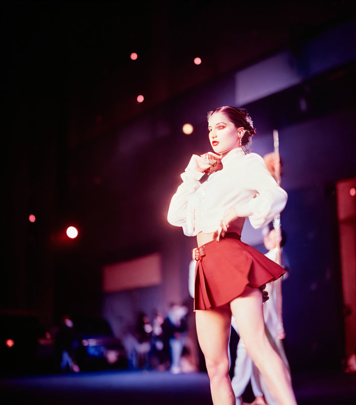 Woman in white blouse and red skirt on stage with dramatic lighting and blurry figures