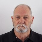 Elderly man with white beard and mustache in black shirt on light background