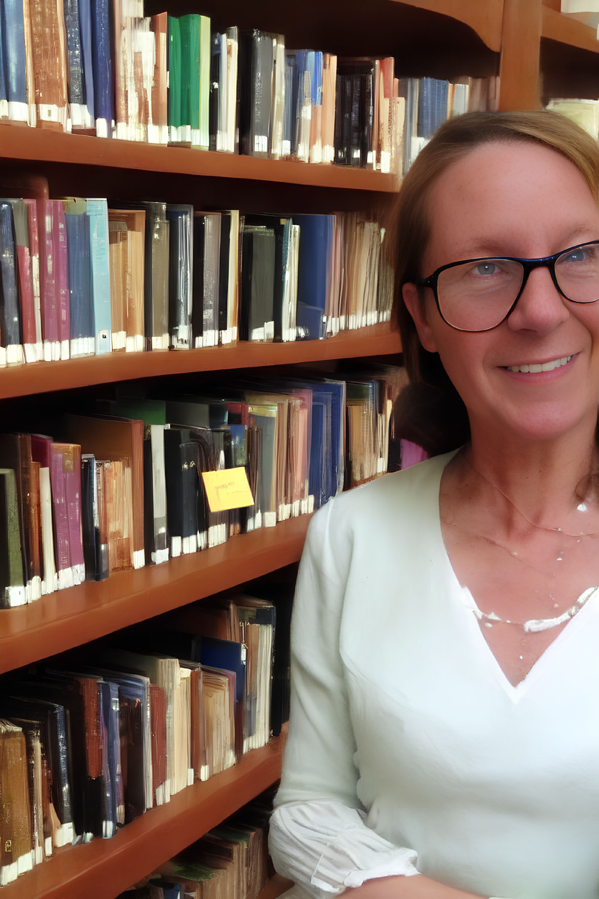 Smiling woman with glasses in well-lit room surrounded by books