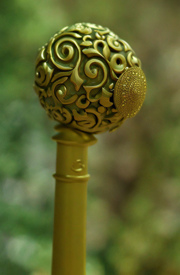 Golden ornate scepter with swirling patterns and textured orb on blurred green background