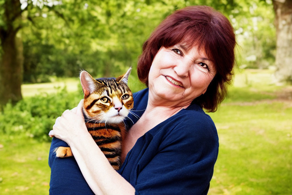 Smiling woman with short reddish hair holding tabby cat outdoors