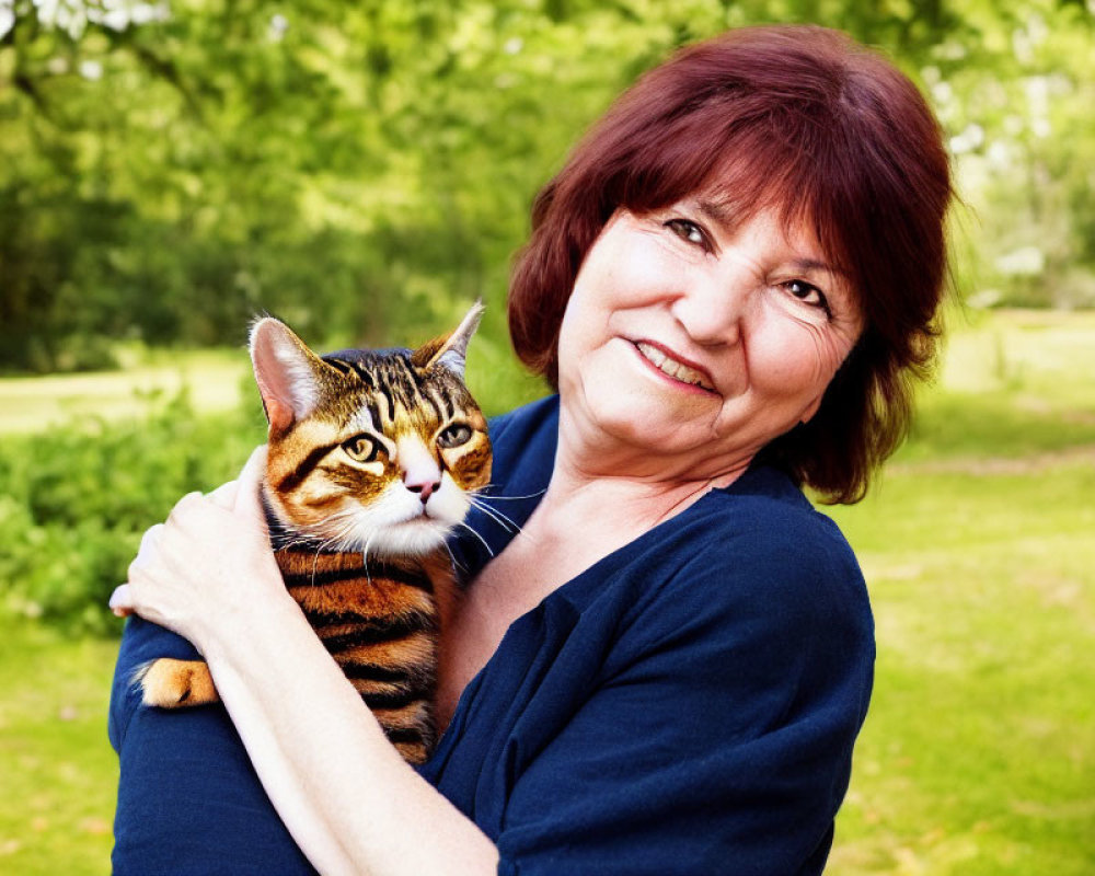 Smiling woman with short reddish hair holding tabby cat outdoors