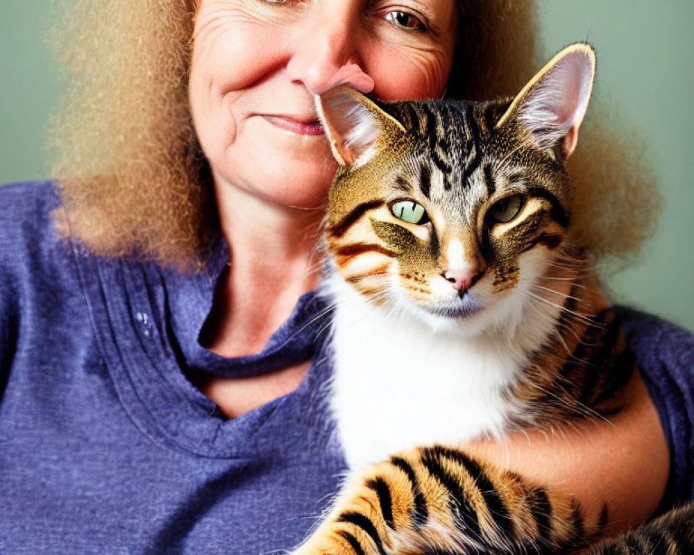 Blonde woman with tabby cat in blue top against green background