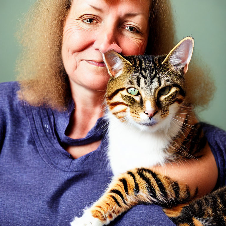 Blonde woman with tabby cat in blue top against green background