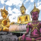 Three Golden Buddha Statues in Various Poses Near Asian Temple