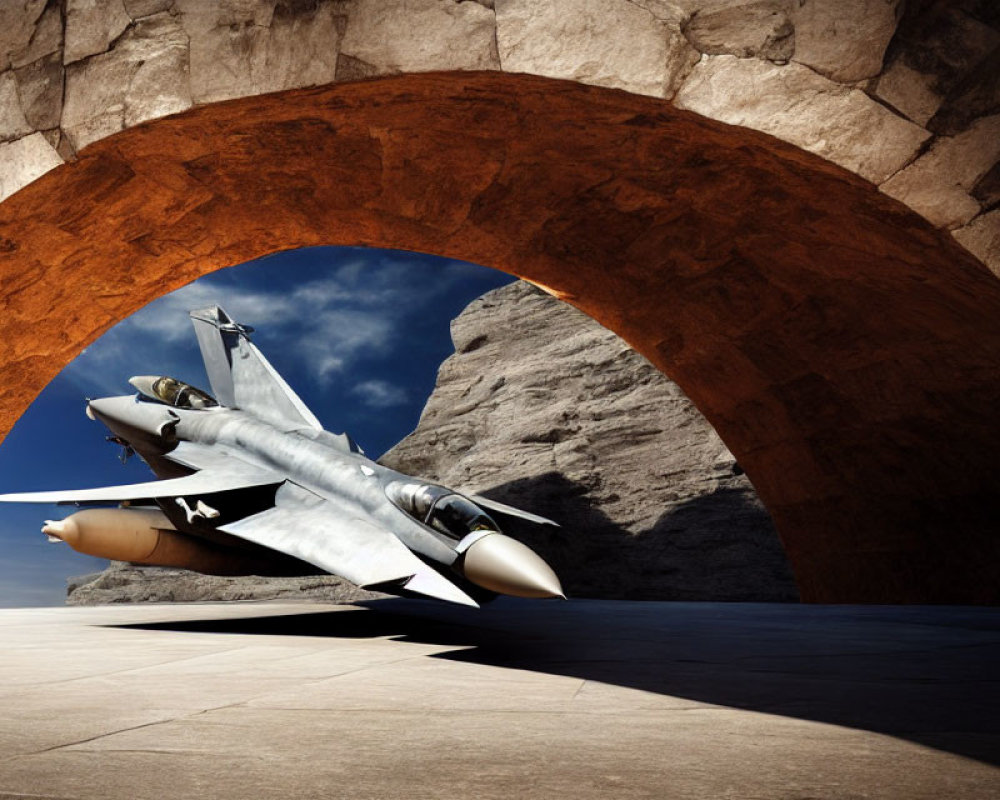 Low-flying fighter jet under large stone arch in clear blue sky
