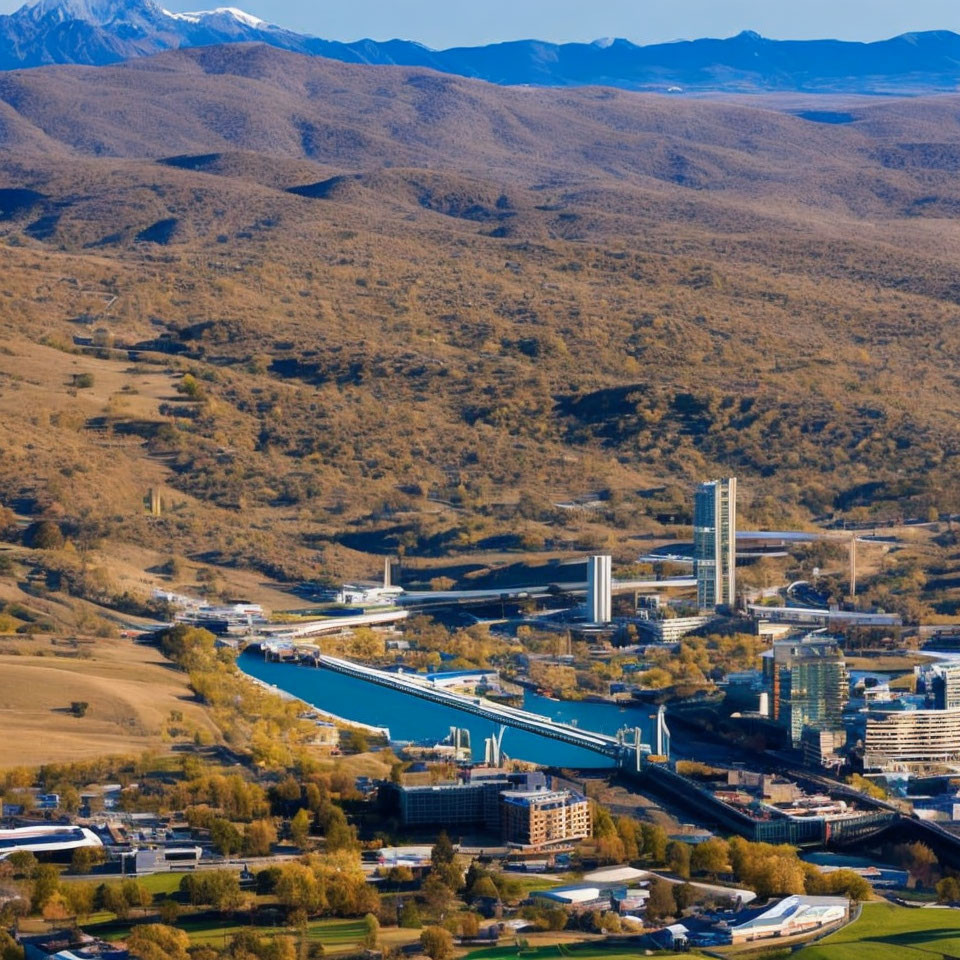 Industrial area with factories, blue canal, hills, and mountains in aerial view