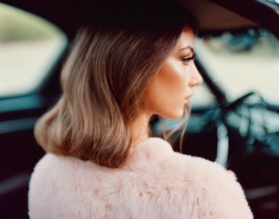 Woman in pink fur coat sitting in car with profile view