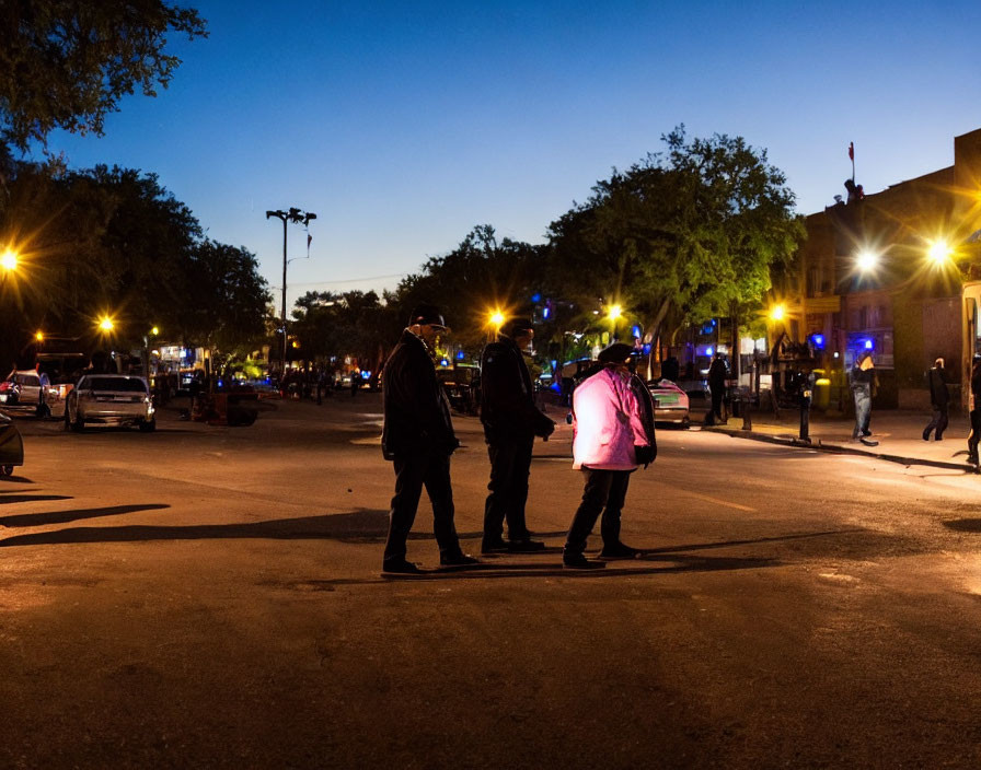 Three People Standing in Urban Street at Dusk with City Lights