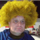 Portrait of a man with blue eyes, beard, yellow afro, against cityscape.