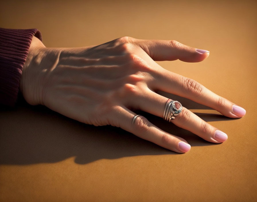 Female hand with pink manicured nails and silver ring on warm beige surface