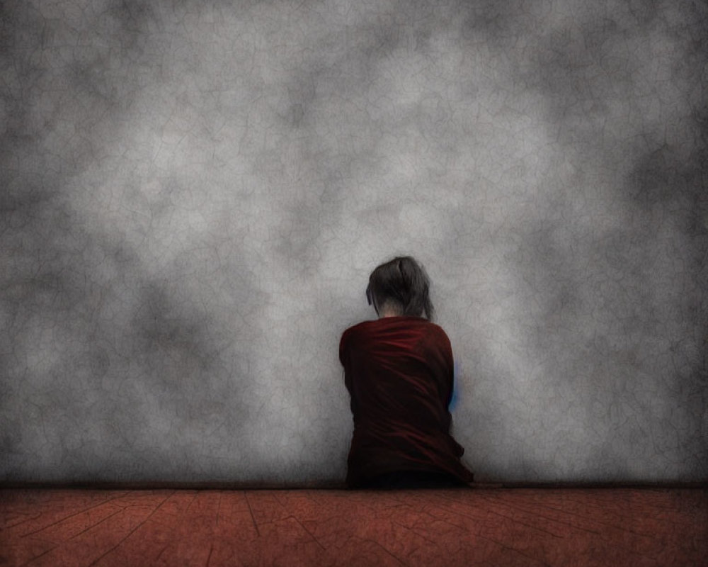 Person in red shirt sitting against textured grey wall.