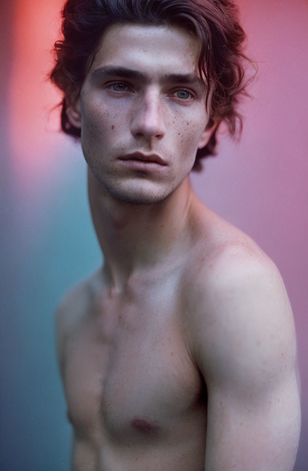 Young man portrait with tousled hair and freckles, shirtless, intense gaze.