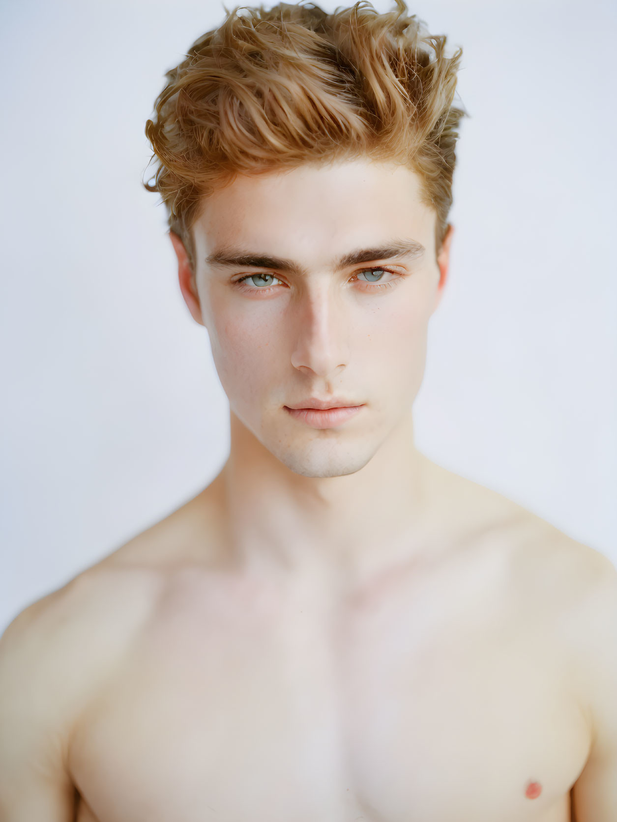 Portrait of young man with tousled brown hair and blue eyes against light background