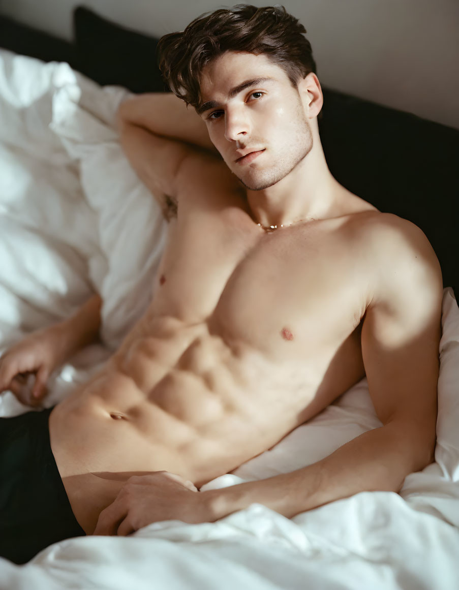 Shirtless young man with toned torso lounging in bed