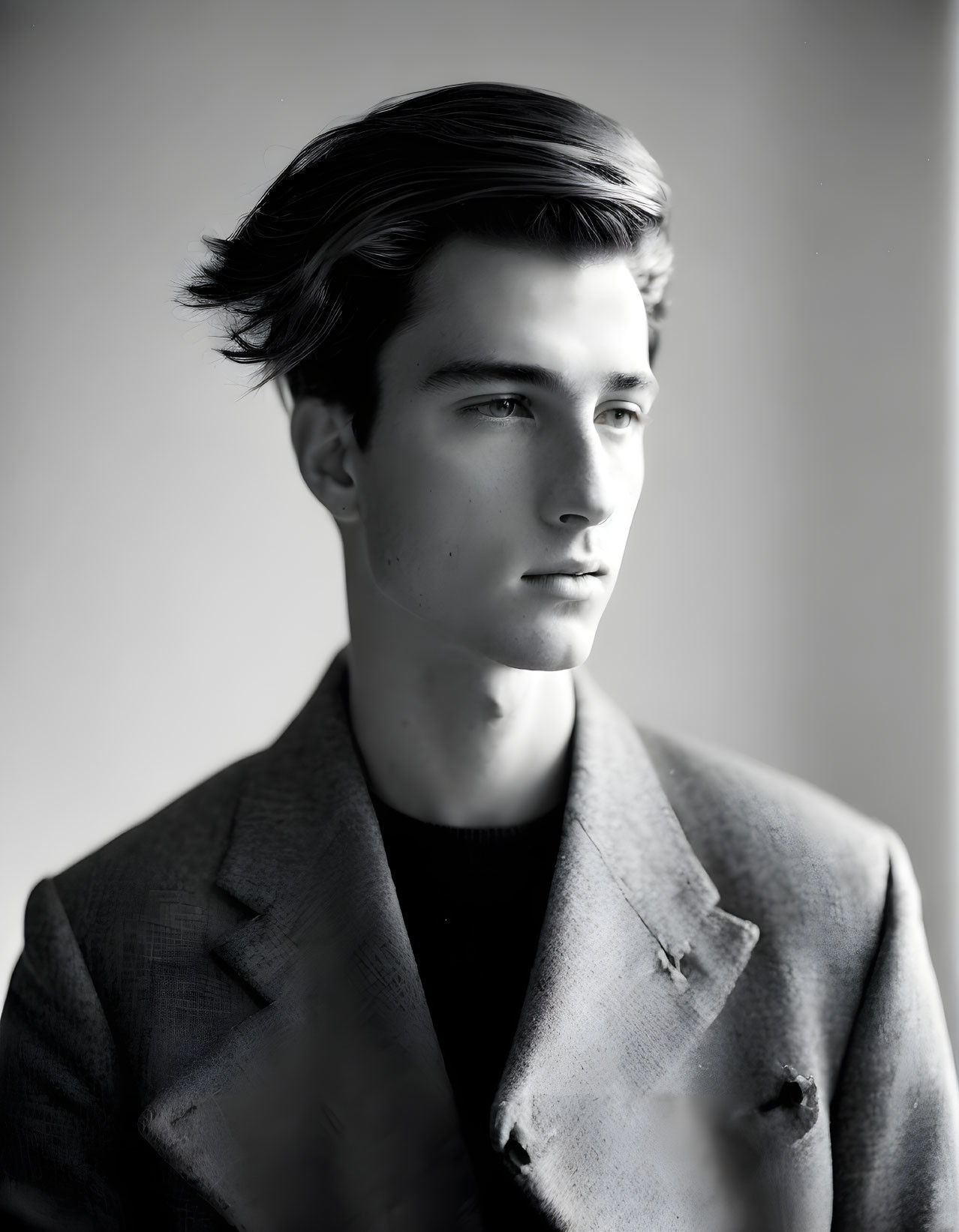 Monochrome portrait of young man in textured blazer, styled hair, gazing sideways