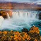 Fantasy landscape with village, waterfalls, boats, river, and castles under warm sky