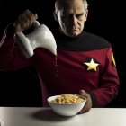 Uniformed person pours milk into cereal bowl against dark backdrop