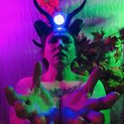 Person with glowing green skin and horns in metallic headpiece on neon backdrop