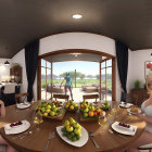 Individuals enjoying a tea party in a sunlit pergola with a view of a tranquil meadow