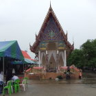 Traditional Thai temple with steep roof and vibrant colors, surrounded by vegetation and two observers