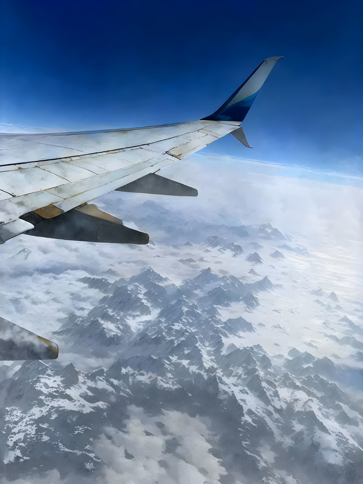 Snow-capped mountains under airplane wing in blue sky