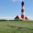 Striped lighthouse with house on rocky coast under blue sky.