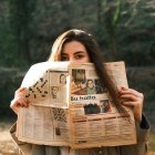 Person reading newspaper outdoors in warm, autumn sunlight.