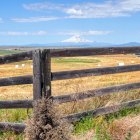 Scenic landscape with wooden fence, golden fields, and snow-capped mountains