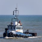 Tugboat near pier with seagulls in blue sea & cloudy sky