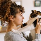 Woman with elegant updo caresses two cats against artistic backdrop