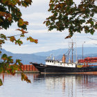 Boat near shore framed by autumn trees, mountains, and cloudy sky