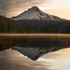 Snow-capped mountain, autumn forest, cabins, and calm lake in serene landscape