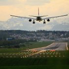 Airplane landing on illuminated runway with mountain backdrop at dusk