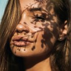 Close-up portrait of woman with sun-kissed skin, water droplets, and leaf shadows.