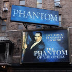 Vintage building facade with "The Phantom of the Opera" billboard featuring man in white half-mask