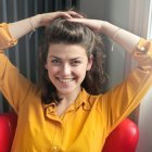 Smiling woman with curly hair in yellow blouse against soft backdrop