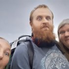 Three people in Viking costumes under cloudy sky, man with beard holding axe.