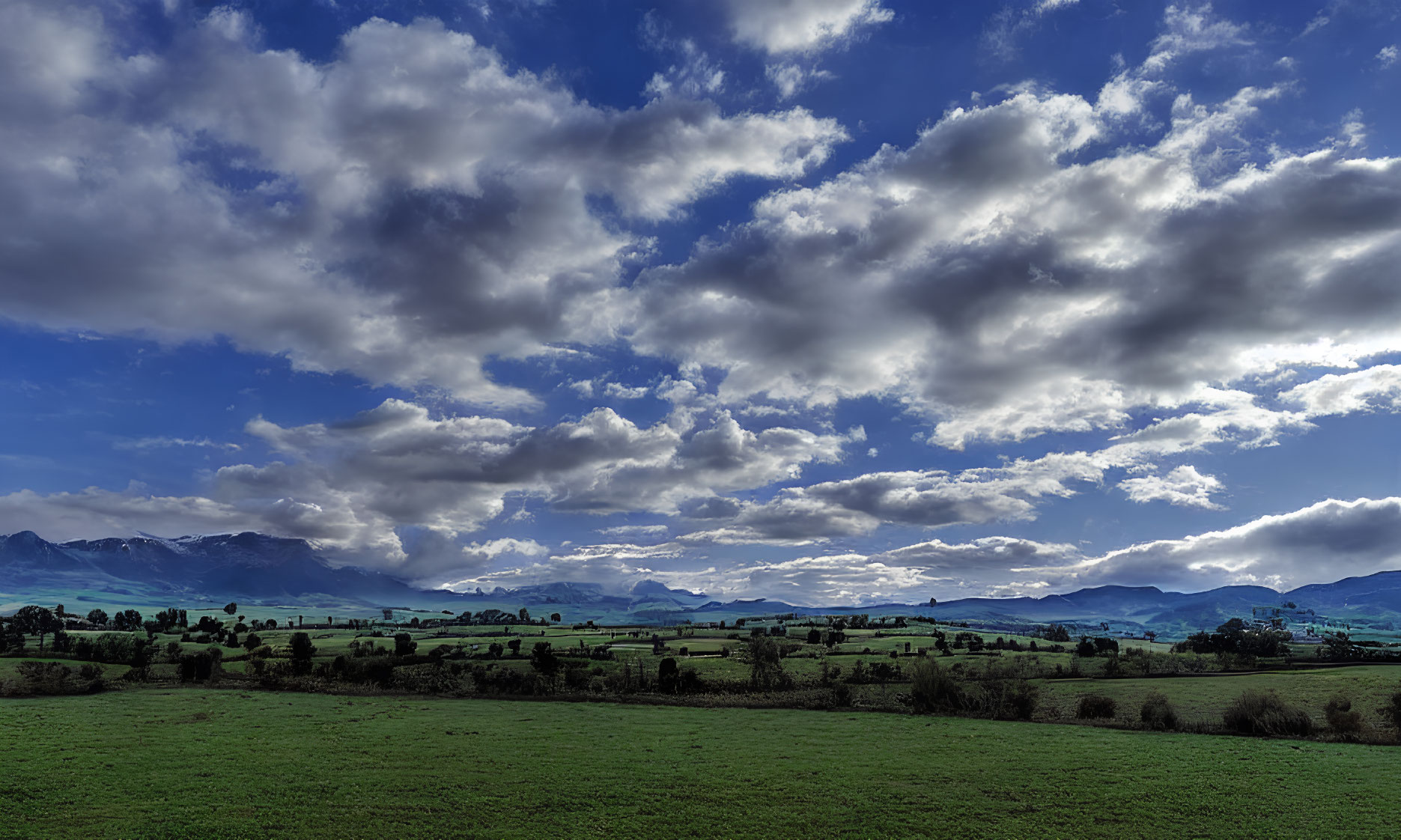 Scenic landscape: green fields, blue sky, mountains.